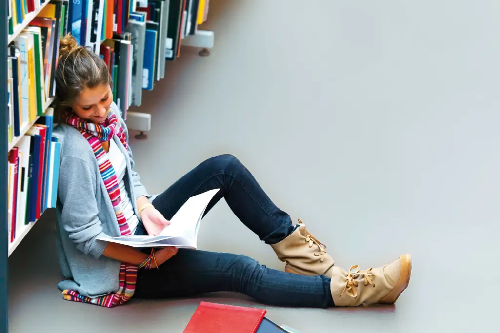 Kvinde læser en bog ved en biblioteksreol